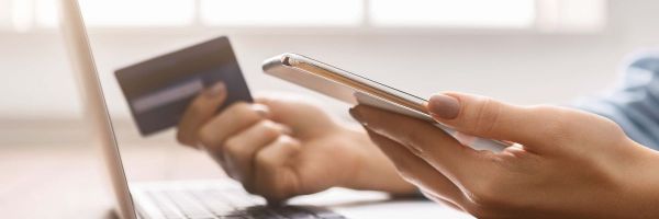 Woman holding mobile phone in one hand and credit card in another whilst working on a laptop